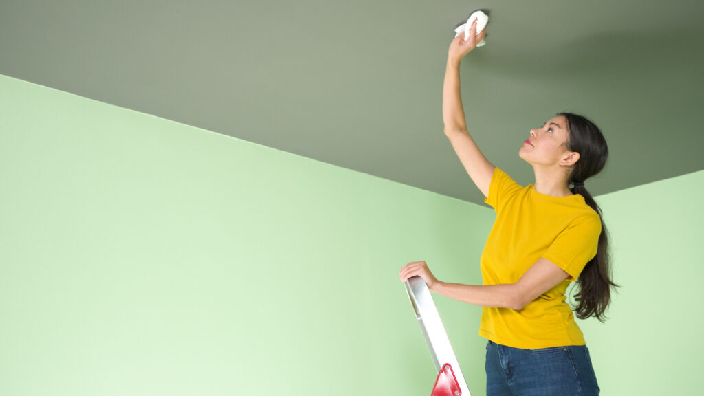 person cleaning and patching the ceiling before spraying and rolling