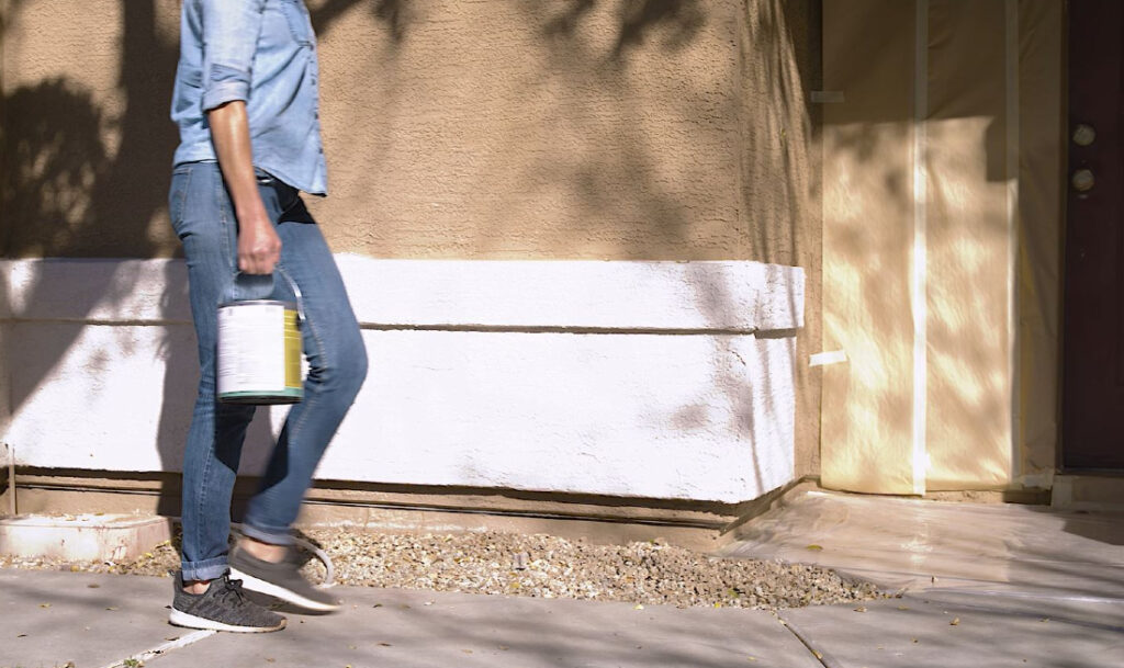 woman carrying paint can to front door 
