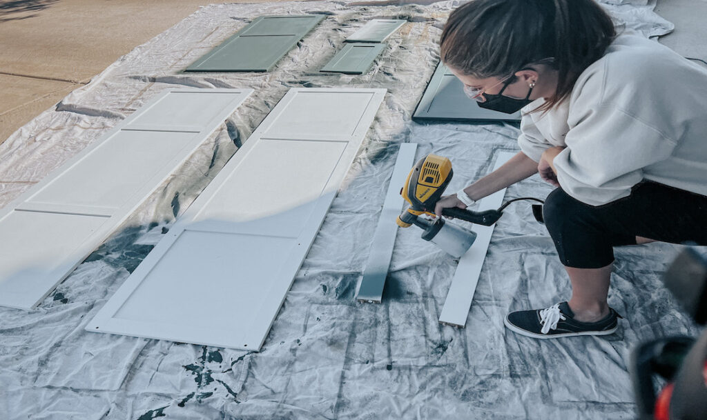 person spraying paint on cabinets outside, kneeling down