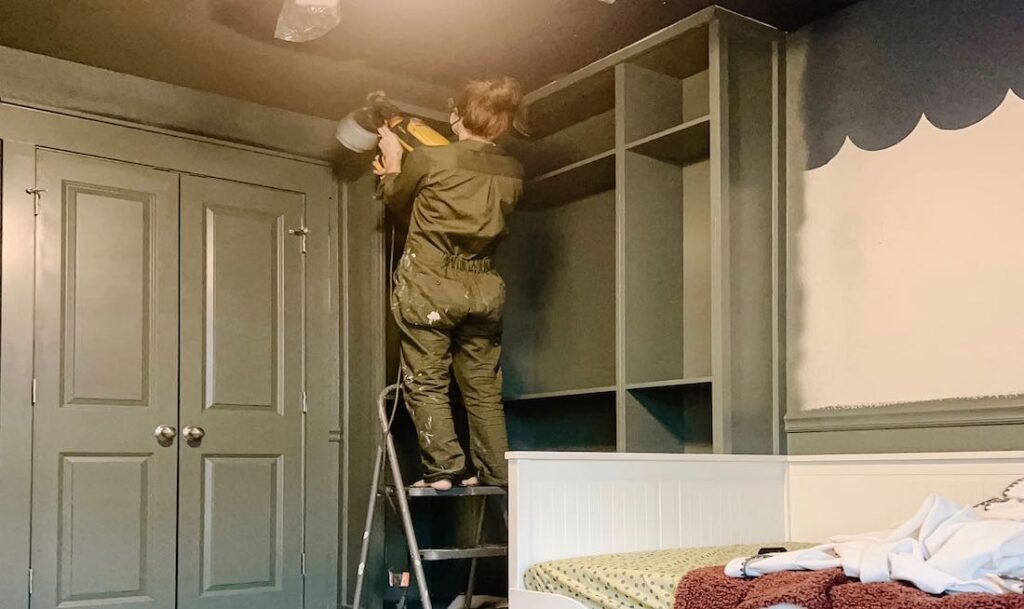 woman painting built in shelves that she installed in the bedroom. Army green paint and outfit