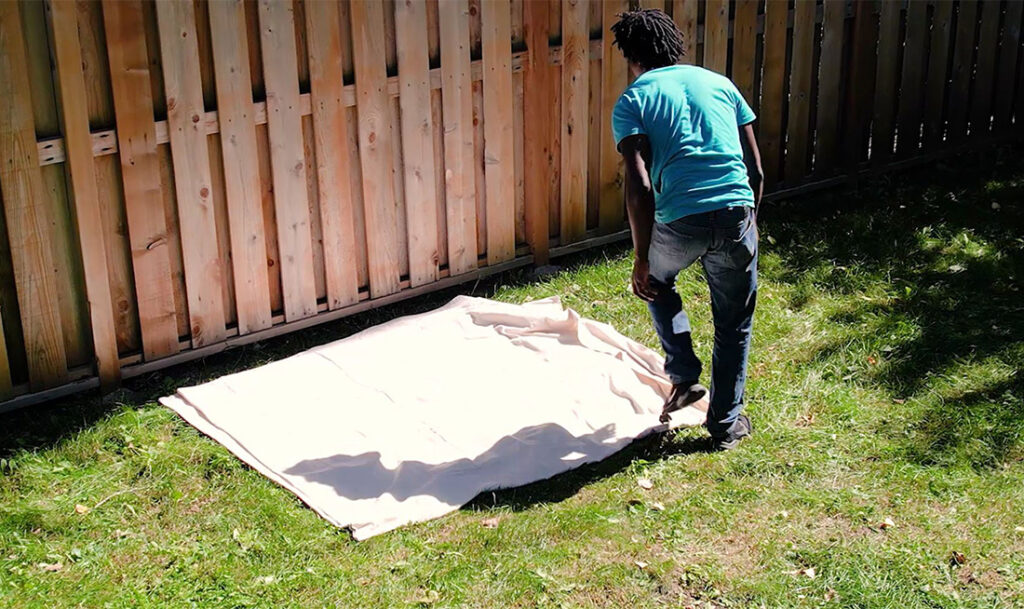 man laying down drop cloth next to fence