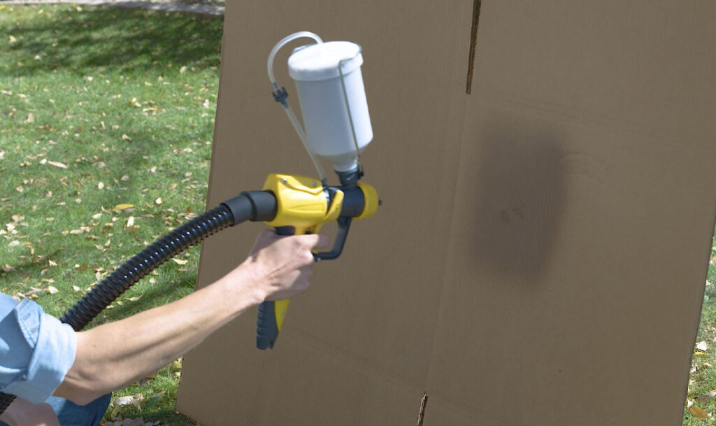 woman practicing spray pattern on piece of cardboard