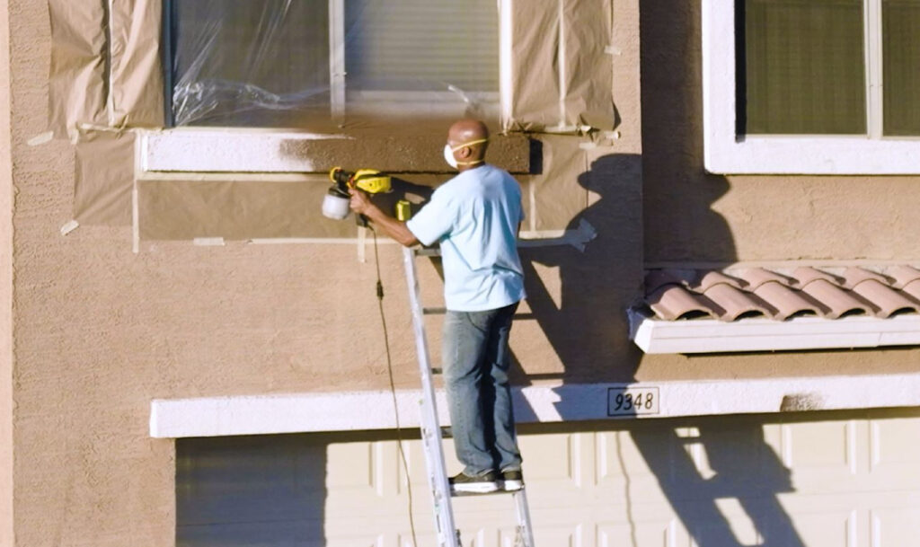 man on ladder spraying home exterior trim